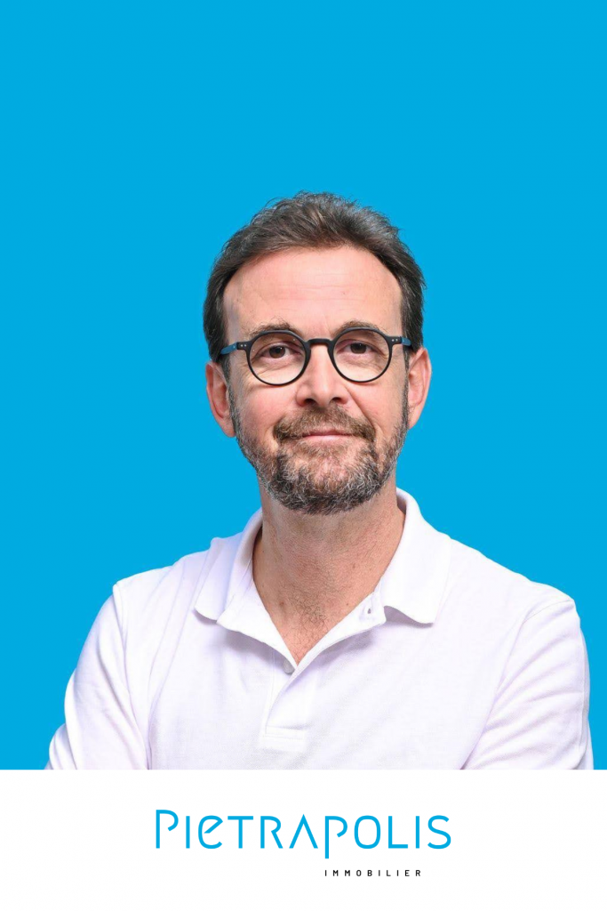 Photo de Sébastien Abeillon, de face. Il est souriant, porte une chemise ainsi qu'une paire de lunettes. Le fond est un bleu uni. En bas de l'image, le logo "Pietrapolis".